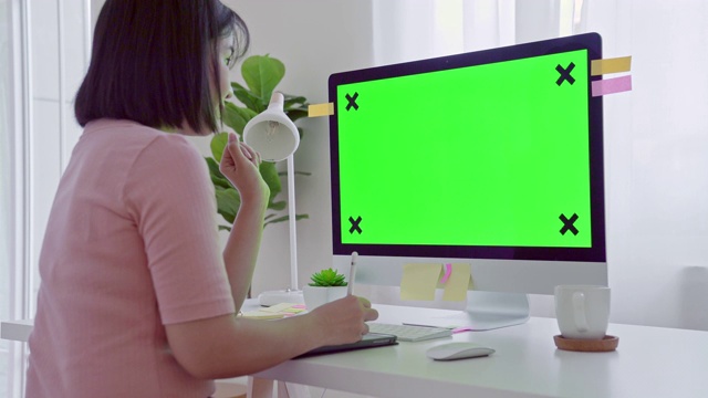 年轻的成年人在她的办公桌前工作在一台模拟绿色屏幕的电脑上。过肩镜头。她坐在家里的书桌前。视频素材