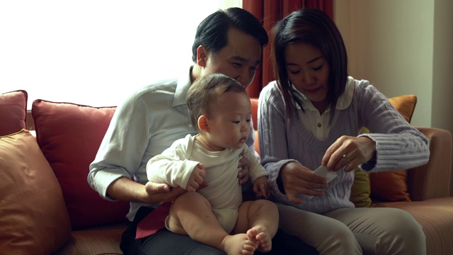 快乐的家庭游戏和婴儿在家里。带着婴儿坐在沙发上享受美好时光的父母。视频下载