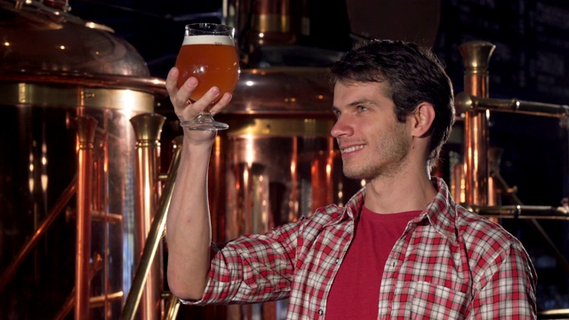 一位开朗的男性酿酒师对着镜头微笑，检查着玻璃杯里的啤酒视频下载