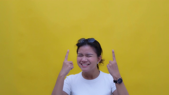 SLO MO肖像的年轻亚洲与一个幸福的微笑指向拷贝空间-手势在黄色的背景视频素材