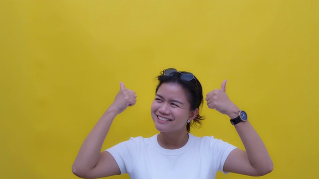 SLO MO肖像的年轻亚洲与一个幸福的微笑给予两个拇指，向上拷贝空间-手势在黄色的背景视频素材