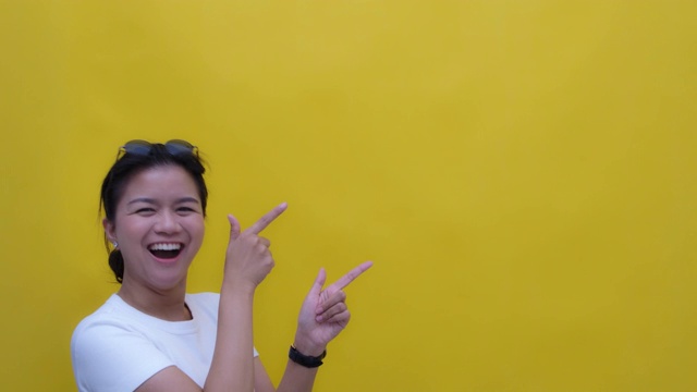 SLO MO肖像的年轻亚洲与一个快乐的微笑指向复制空间-手势在黄色的背景视频素材