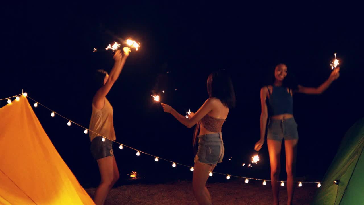 快乐的闺蜜女团在海滩玩烟花，友谊的概念与年轻的女性朋友享受时间，有真正的乐趣在露营视频素材