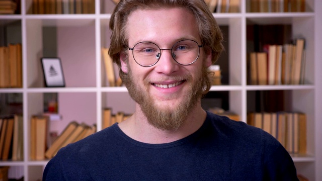 这张照片拍摄的是一位戴着眼镜的成年帅气男学生，他在大学图书馆里开心地看着镜头视频素材