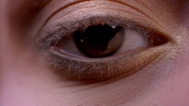特写半脸拍摄的女性脸与棕色眼睛直视相机，眨眨眼睛与化妆应用视频素材