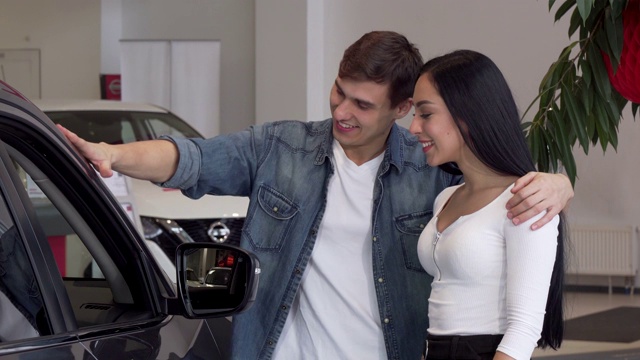 一对年轻夫妇在汽车经销店挑选新车，看着车里面视频下载