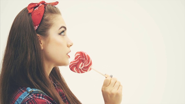 漂亮的海报女郎站在侧面，舔着红色的心形棒棒糖，脸上洋溢着喜悦的表情。视频下载
