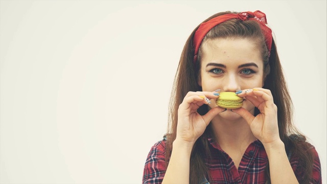 漂亮的年轻时髦的女孩拿着黄色美味的杏仁饼干在她的嘴前，抬高她的眉毛。视频素材