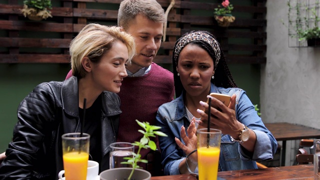 朋友们坐在城市咖啡馆里，一边聊天一边看智能手机视频素材