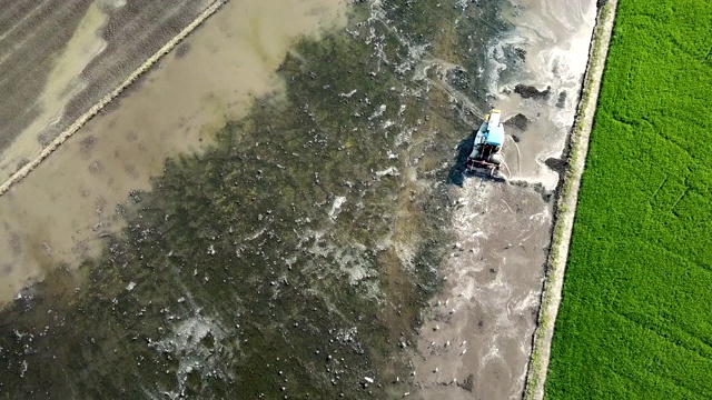 拖拉机在稻田前用犁犁地的鸟瞰图视频素材