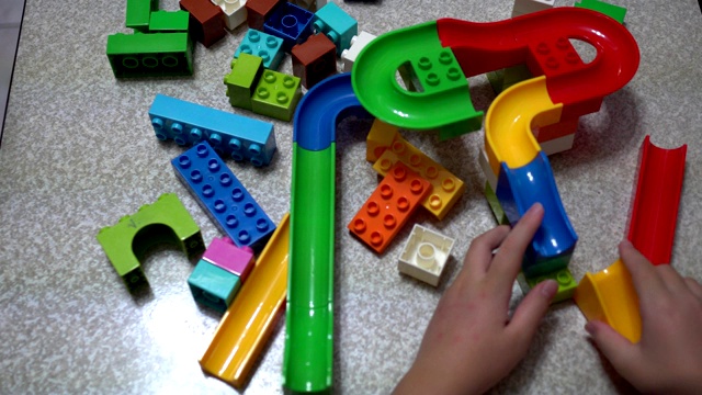 小孩子在玩积木做的轨道。室内有许多五颜六色的塑料玩具。在看。视频下载