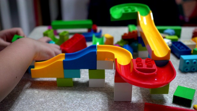 小孩子在玩积木做的轨道。室内有许多五颜六色的塑料玩具。视频下载