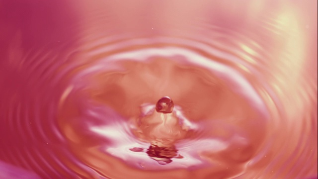 在近距离和慢镜头中，水滴在一个橙色的水坑上激起涟漪视频下载