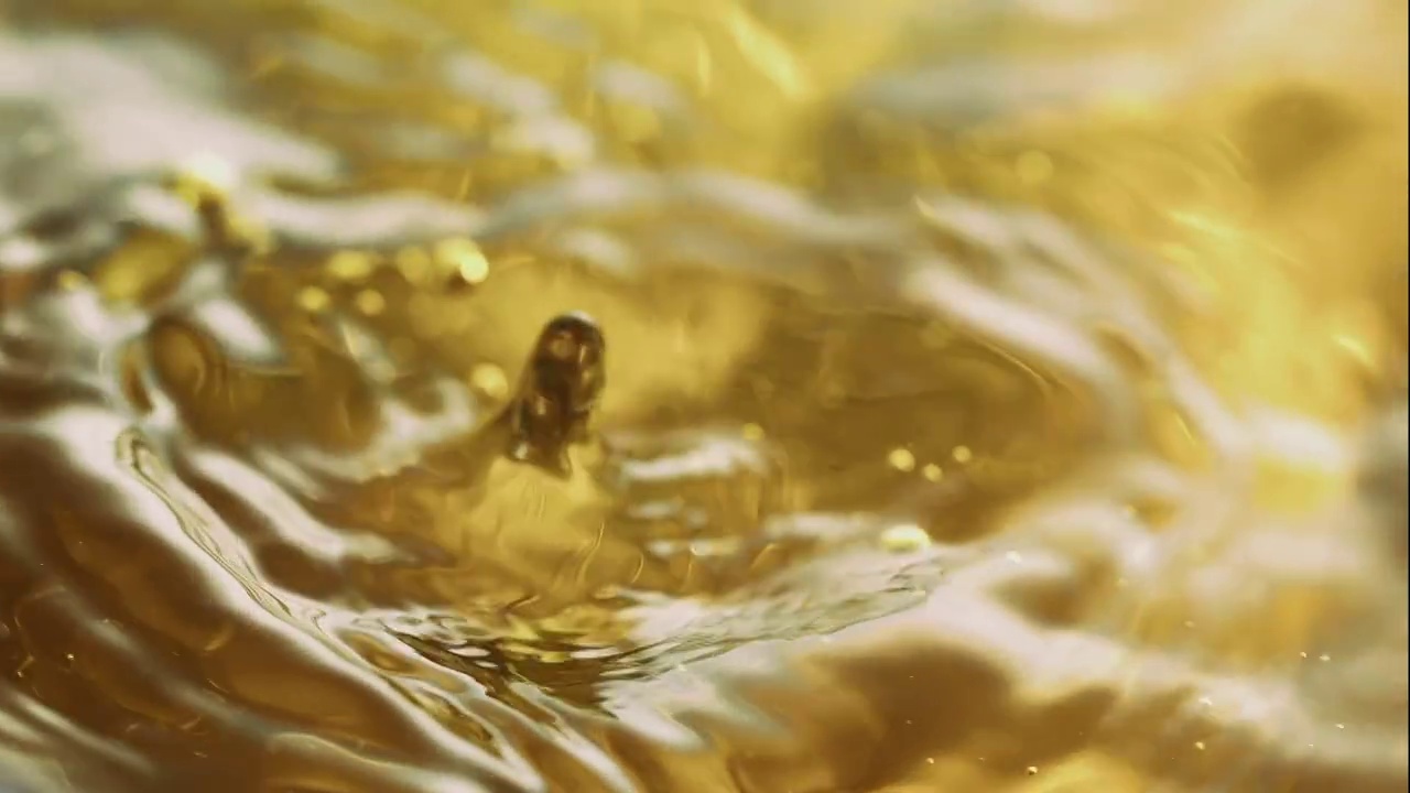 在近距离和慢动作中，水珠在金色的水面上激起涟漪和波浪视频素材