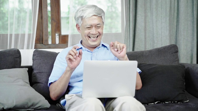 慢镜头:亚洲老人用电脑笔记本电脑查看好消息，心情愉快。视频素材