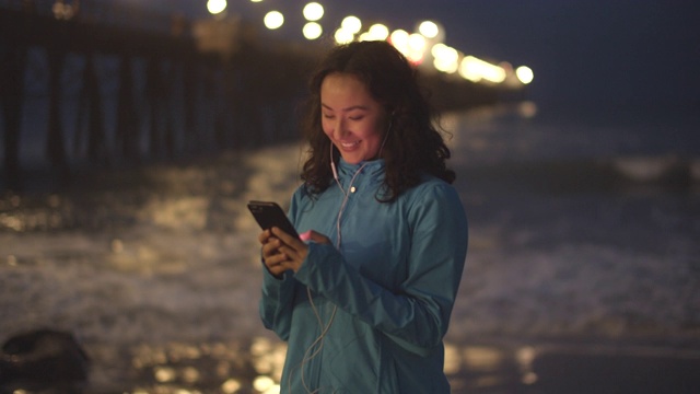 年轻的亚洲女人在晚上在海滩上发短信视频素材