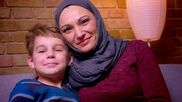 小男孩和他的穆斯林母亲戴着头巾在家里玩耍，他们的鼻子和头互相倾斜。视频下载