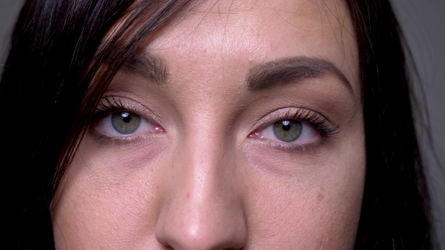 特写的成年白人黑发女性的脸与眼睛看相机与背景孤立在灰色视频素材