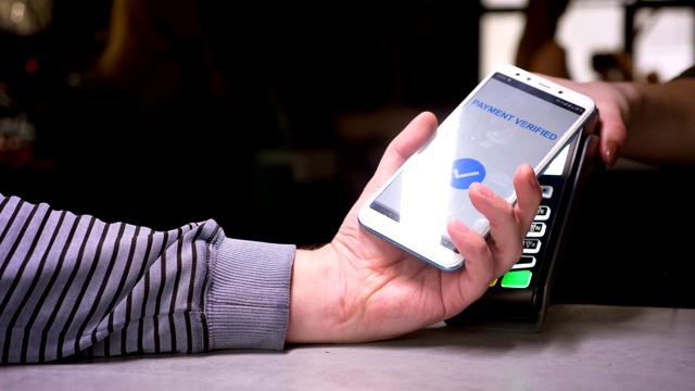 男子将智能手机连接到进行非接触式支付的终端上，在健身房后台喝一杯咖啡。视频素材