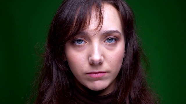 年轻的黑发女学生的肖像与平静的悲伤进入镜头上的绿色背景。视频下载