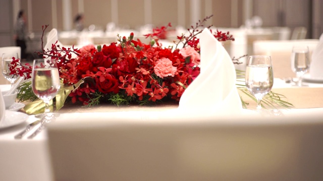 2 MS Dolly右镜头婚礼餐桌的镜头设置在红色鲜花模糊的背景下聚焦在酒杯上。视频下载