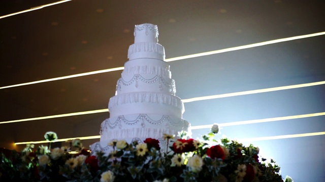 在明亮的灯光背景下，用鲜花装饰的白色婚礼蛋糕。视频下载