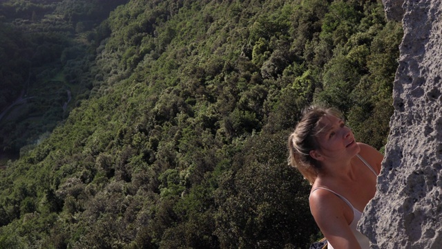 年轻女子攀登垂直岩壁，在森林之上视频素材
