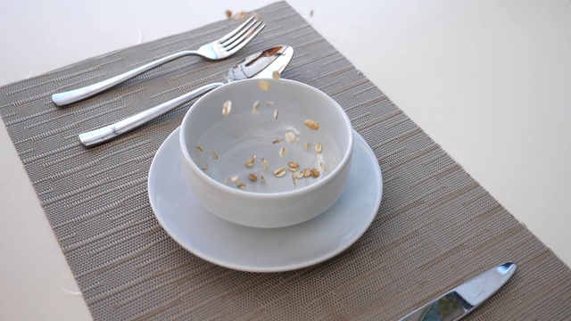 健康早餐，干脆的麦片落进碗里。碗的细节图，桌上有玉米片和刀叉。健康食品的概念。慢镜头视频下载