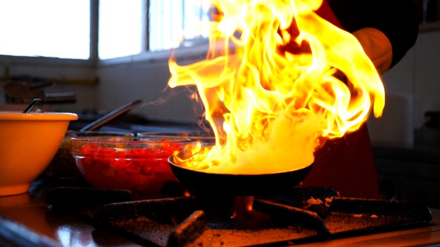 面目全非的厨师烹饪美味的火焰风格的菜在平底锅为客人的餐厅。专业的厨师在火红的煎锅上混合和煎蔬菜。侧视慢动作特写视频下载