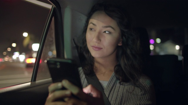 一名年轻女子坐在一辆车的后座上发短信视频素材