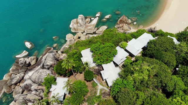 热带岛屿上的小房子。阳光明媚的泰国，苏梅岛海岸上的小平房，靠近平静的海面。火山岩石和悬崖无人机俯视图。视频下载