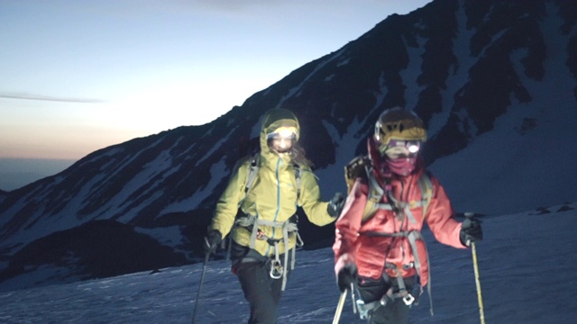 母亲和女儿的登山运动员在黎明攀登雪山脊视频下载