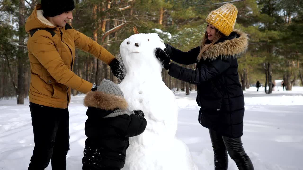 快乐的家庭妈妈，爸爸和儿子在冬季城市公园堆雪人。视频素材