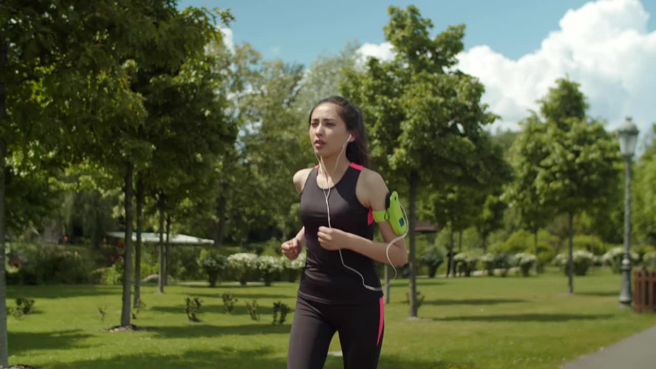 戴着耳机的女人在公园车道上跑步视频下载