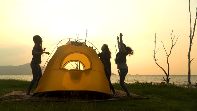 低角度视角:三个年轻女人的剪影成功地在周末一起搭帐篷露营视频下载