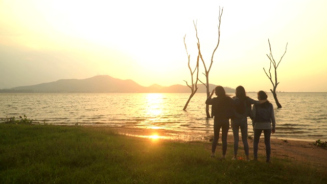 一群年轻女子紧密地站在水边看日落视频素材