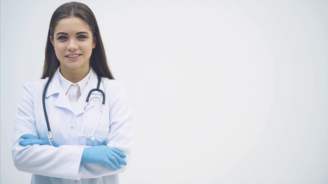 年轻的女实习生站在医疗制服，看着镜头，微笑，她的手交叉。视频下载