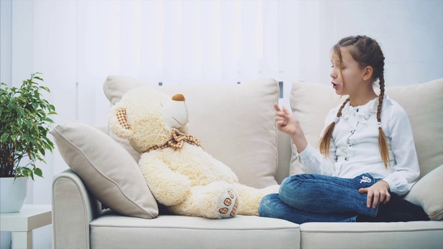 可爱的小女孩坐着，和她的泰迪熊聊天，责骂它，摇她的头和手指。视频下载
