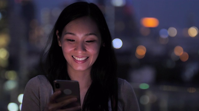 年轻的亚洲迷人的女人用智能手机在城市的夜晚小镇视频下载