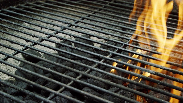 一名白人男子的手把一根点燃的木火柴扔进一个户外烧烤架，点燃煤块，准备烧烤视频素材