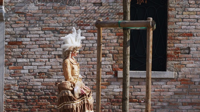穿着古装和威尼斯面具的妇女走在砖房旁视频素材