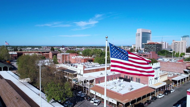 老萨克拉门托和遥远的萨克拉门托市中心前飘扬的美国国旗。无人机低空视频与轨道摄像机运动。视频下载