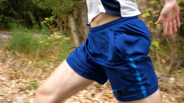 年轻强壮的运动员在森林附近的小道上快速奔跑的特写。初秋，一个运动健将在户外慢跑。英俊的男人在大自然中奔跑。健康积极的生活方式概念。升降镜头视频下载