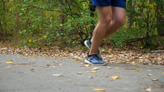 初秋，年轻运动员沿着森林附近的小路快速短跑的男性双腿。在大自然的道路上奔跑的运动员的脚。强壮的运动员在户外慢跑。健康积极的生活方式。低的观点视频素材