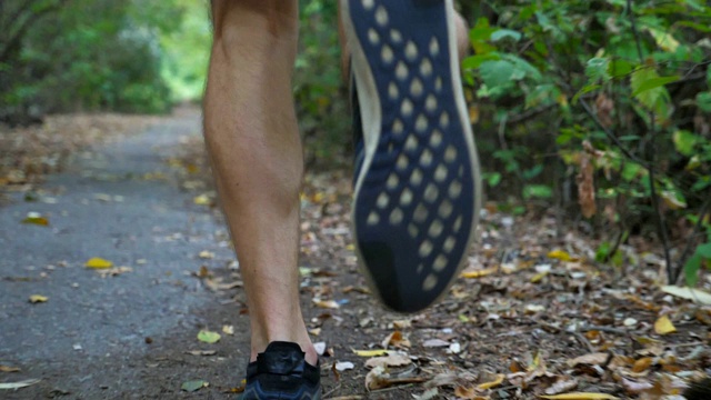 在初秋的森林里，年轻运动员的脚沿着小道奔跑。在大自然中沿着小路慢跑的运动员的双腿。跟随户外运动员训练。健康积极的生活方式。后视视频素材