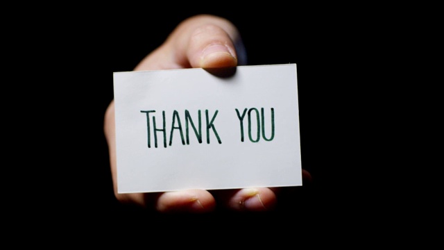 一只手在黑色背景上孤立地展示着一张写着“谢谢你”的卡片。视频下载
