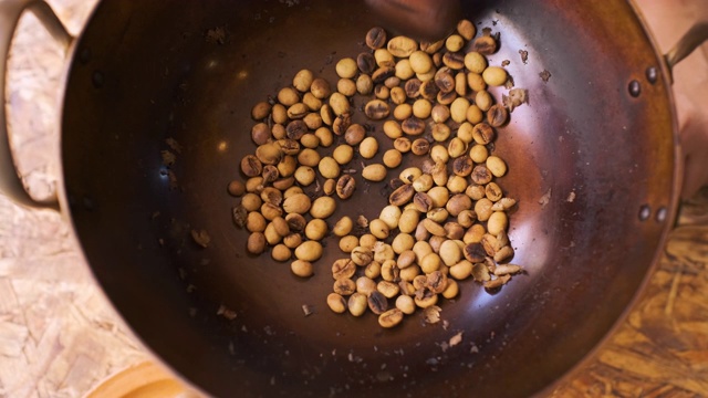 慢镜头近距离拍摄用木勺在平底锅里烘焙新鲜咖啡豆，准备自制咖啡视频下载