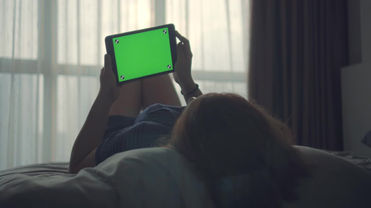 年轻女性在床上使用数码平板电脑，绿色屏幕视频素材