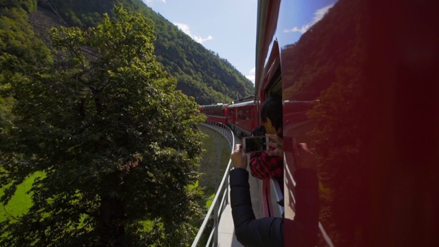 游客们用手机拍下红色火车和崎岖山脉的一侧——瑞士的阿尔卑斯山视频素材