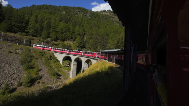 红色火车的一边，因为它蜿蜒在一个黑暗的封闭桥上树木繁茂的曲线-瑞士阿尔卑斯山，瑞士视频素材